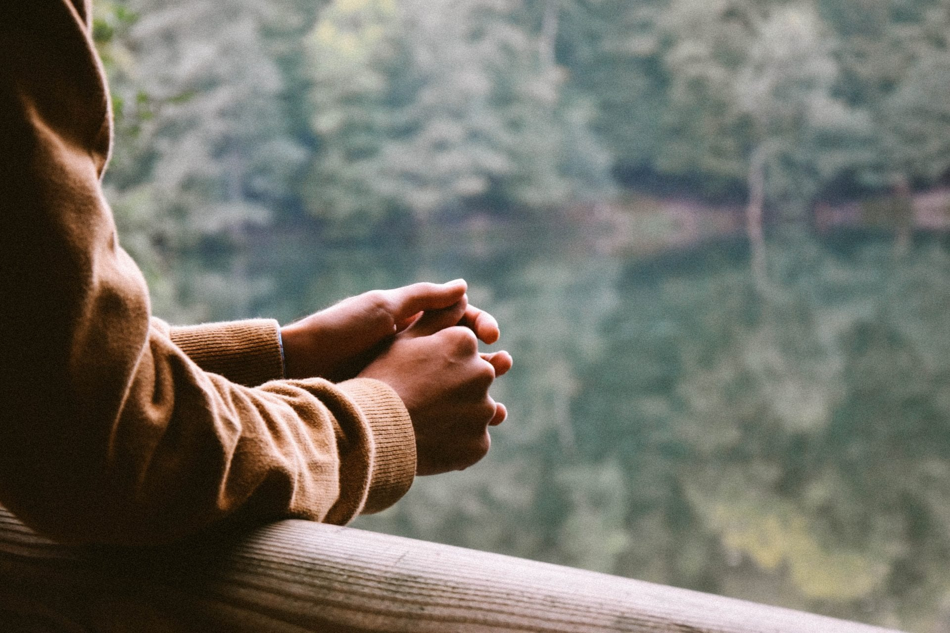 hands leaning on a wood railing over looking a lake
