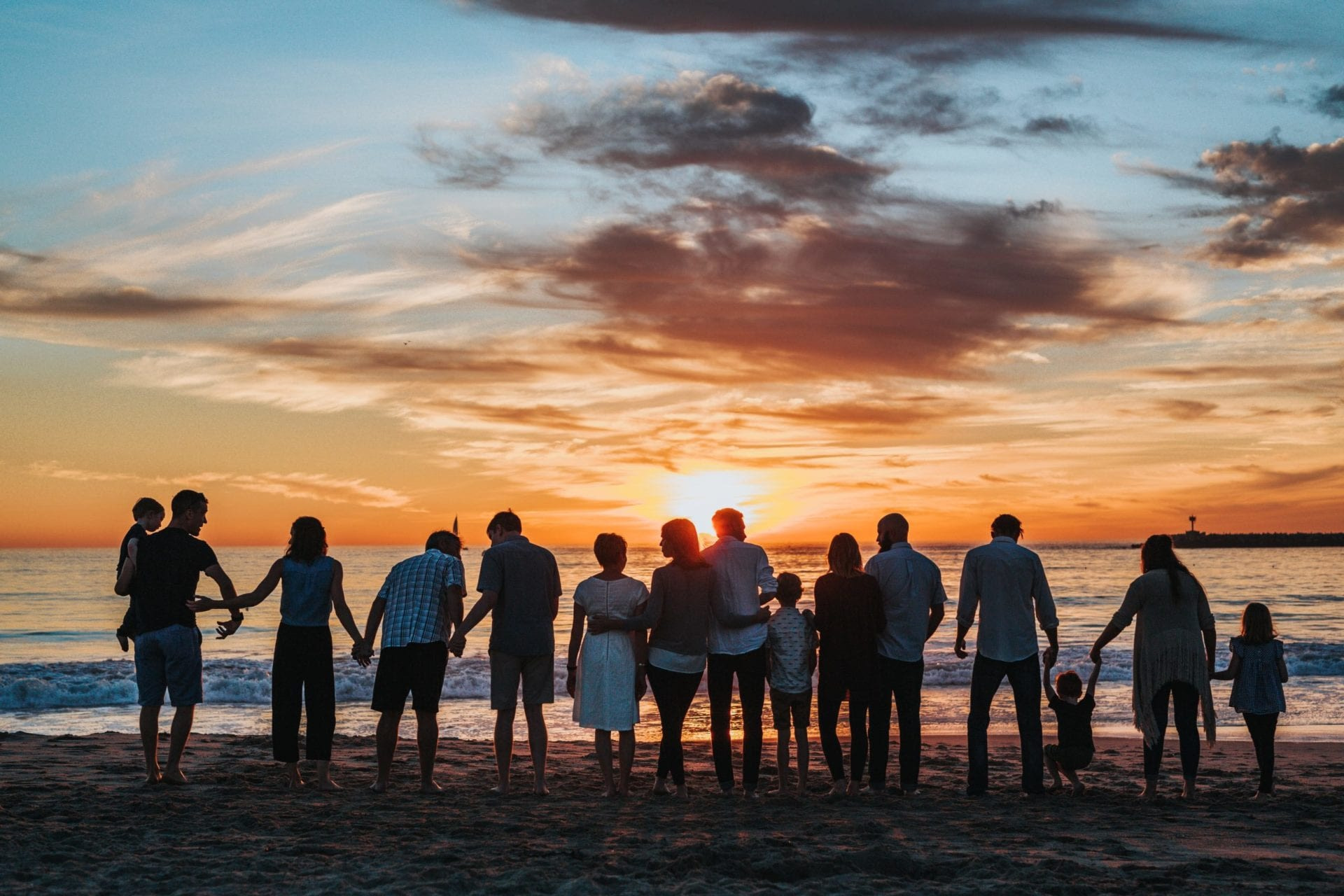 A group of people standing on the beach at sunset