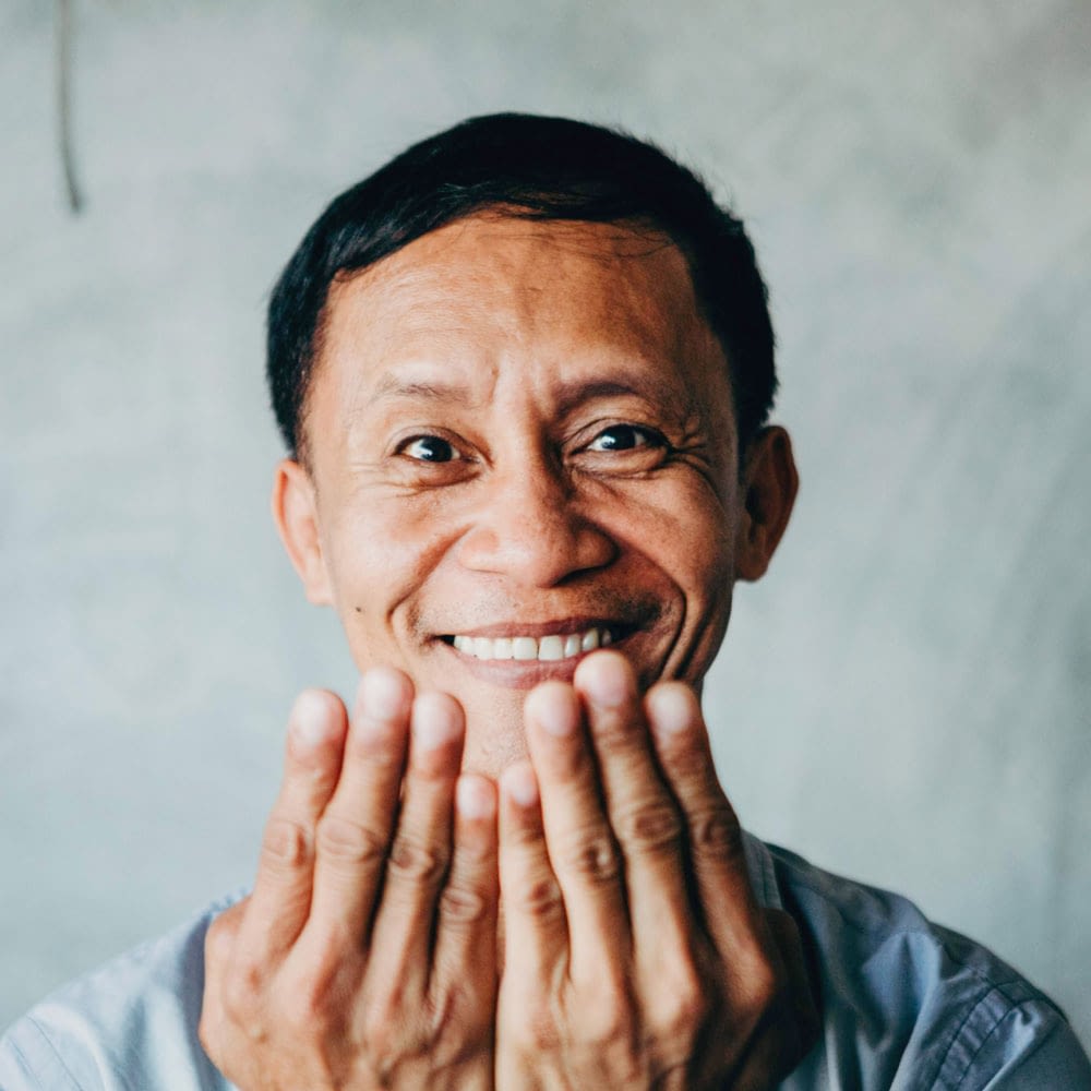 Smiling person holding hands near face, joyful expression.