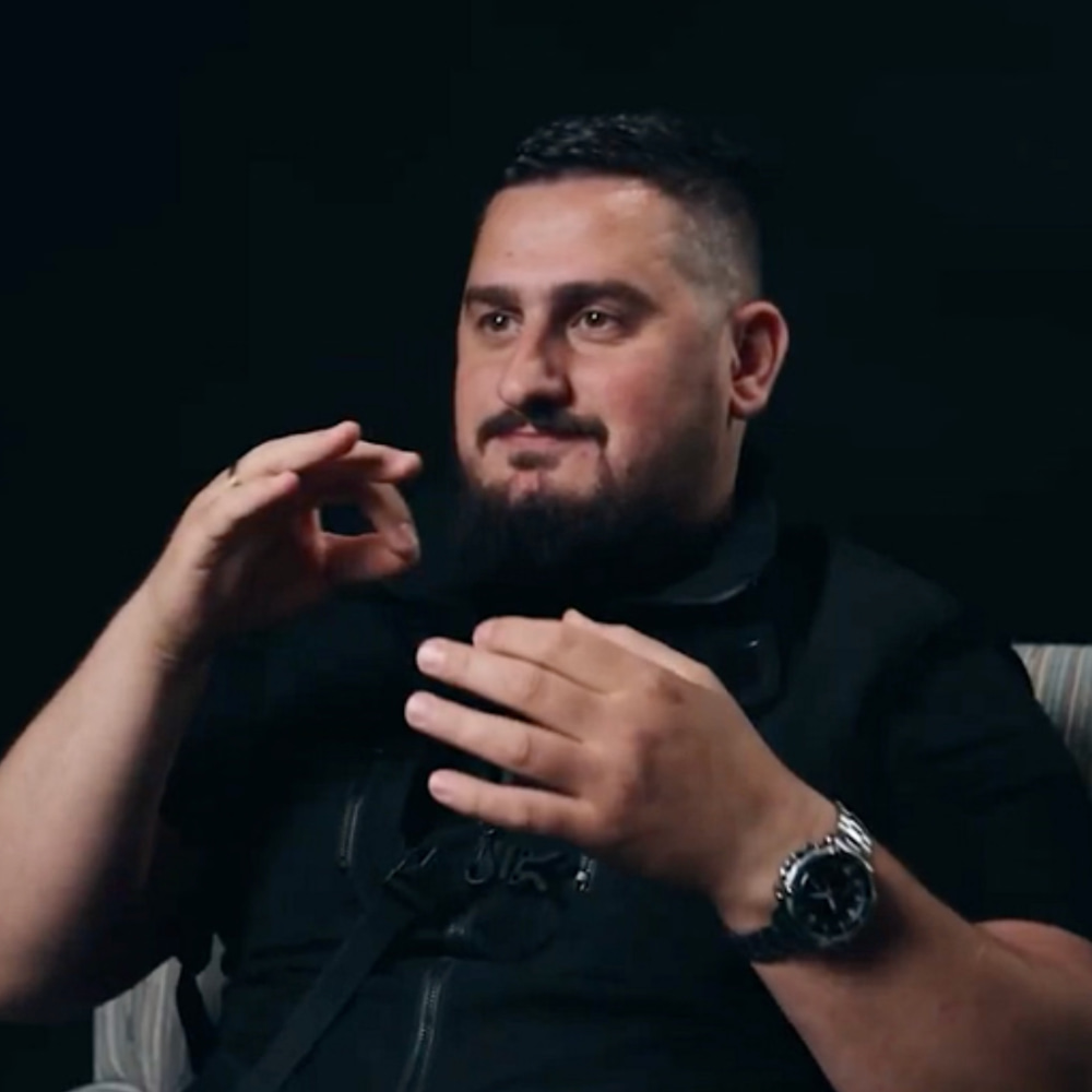 Man using sign language in an interview against a black background.