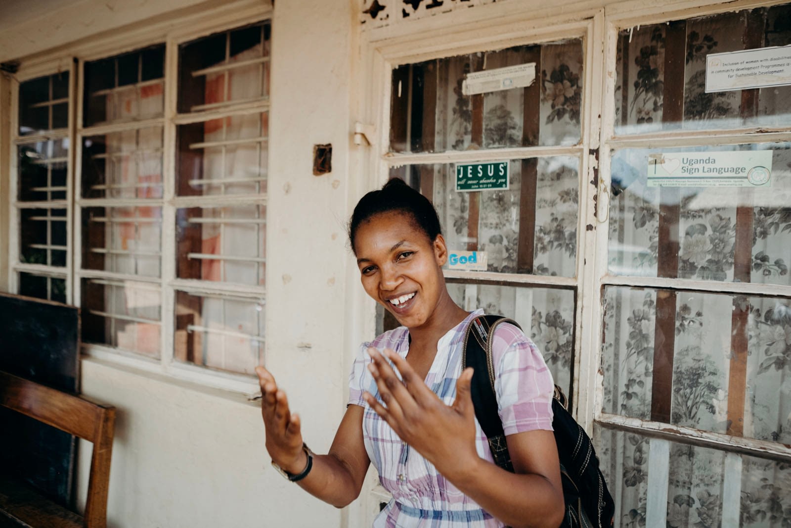 Smiling woman outside building with sign language posters.