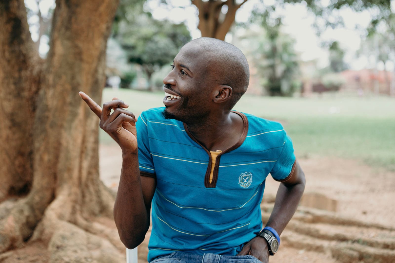 Man smiling and pointing while sitting outdoors.