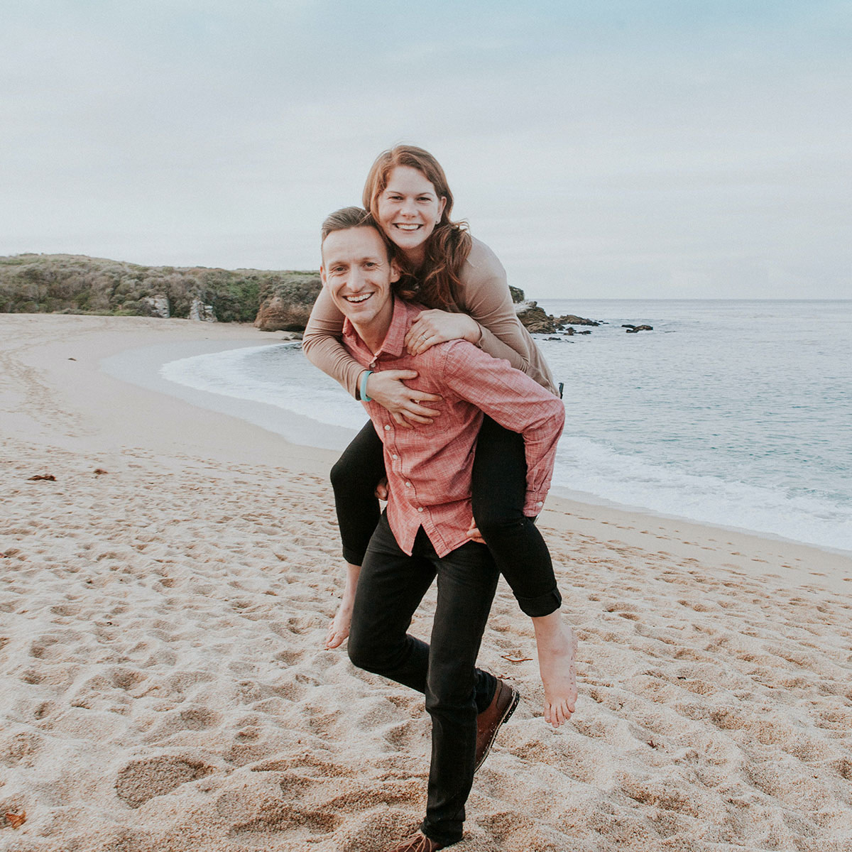 Younger couple in nice clothes at the beach. Man is carrying woman piggyback style.