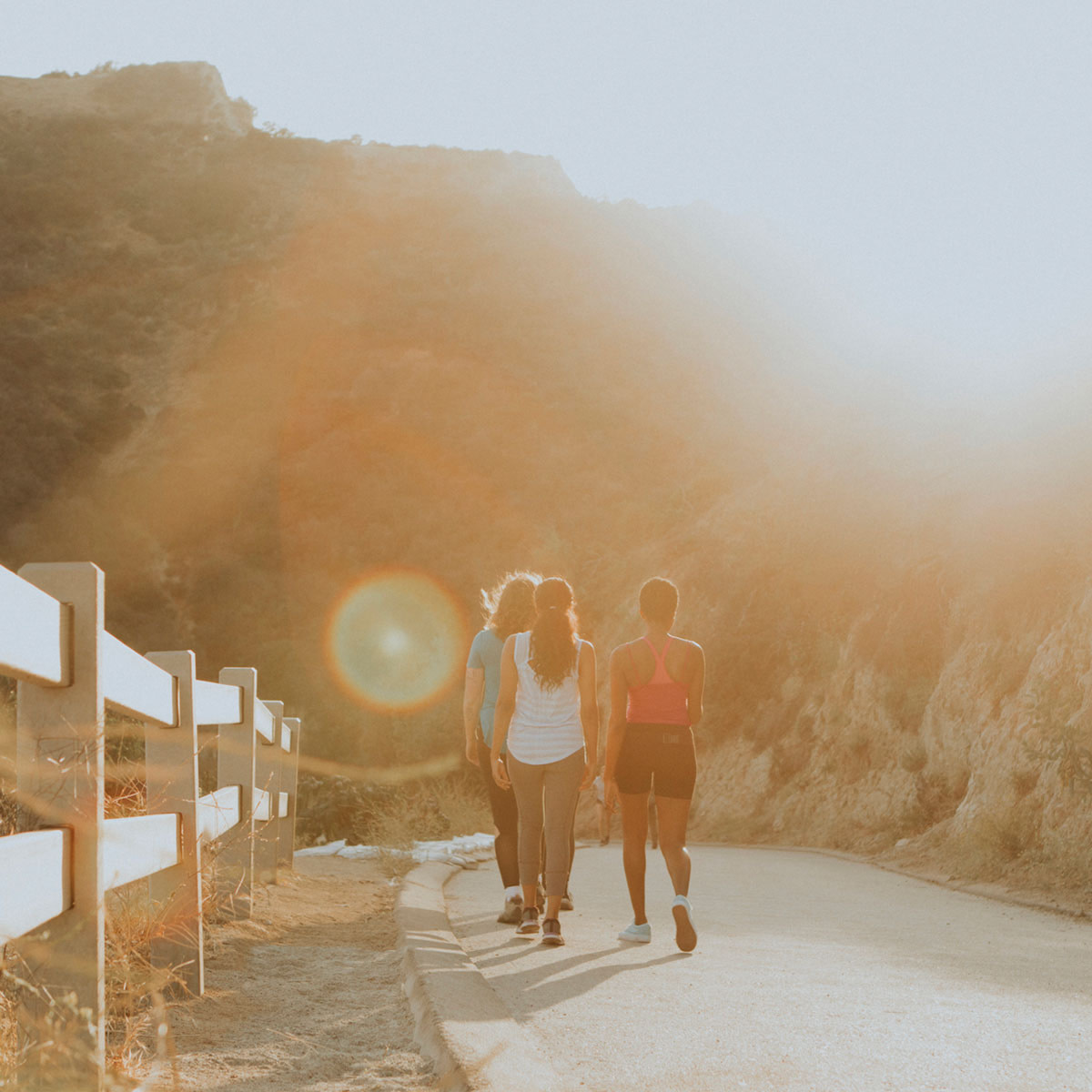 Three women hiking down a paved urban trail into a golden light