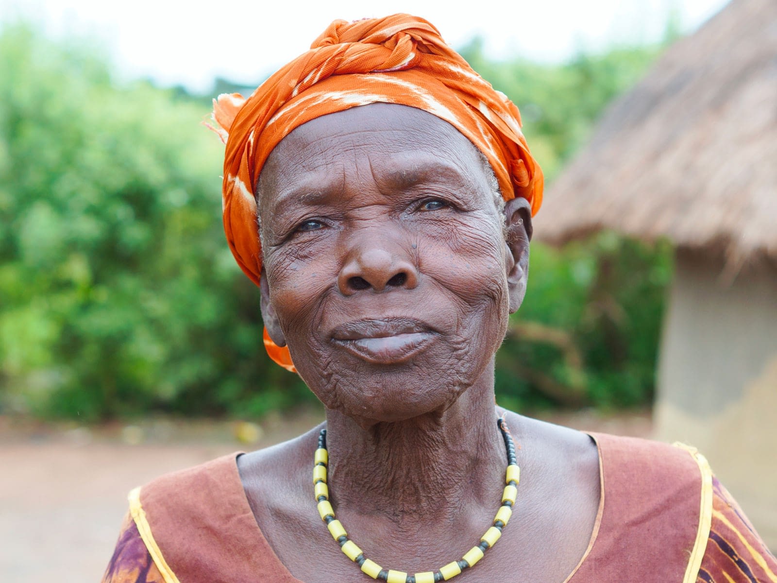 Woman wearing necklace and head scarf in front of building with thatched roof