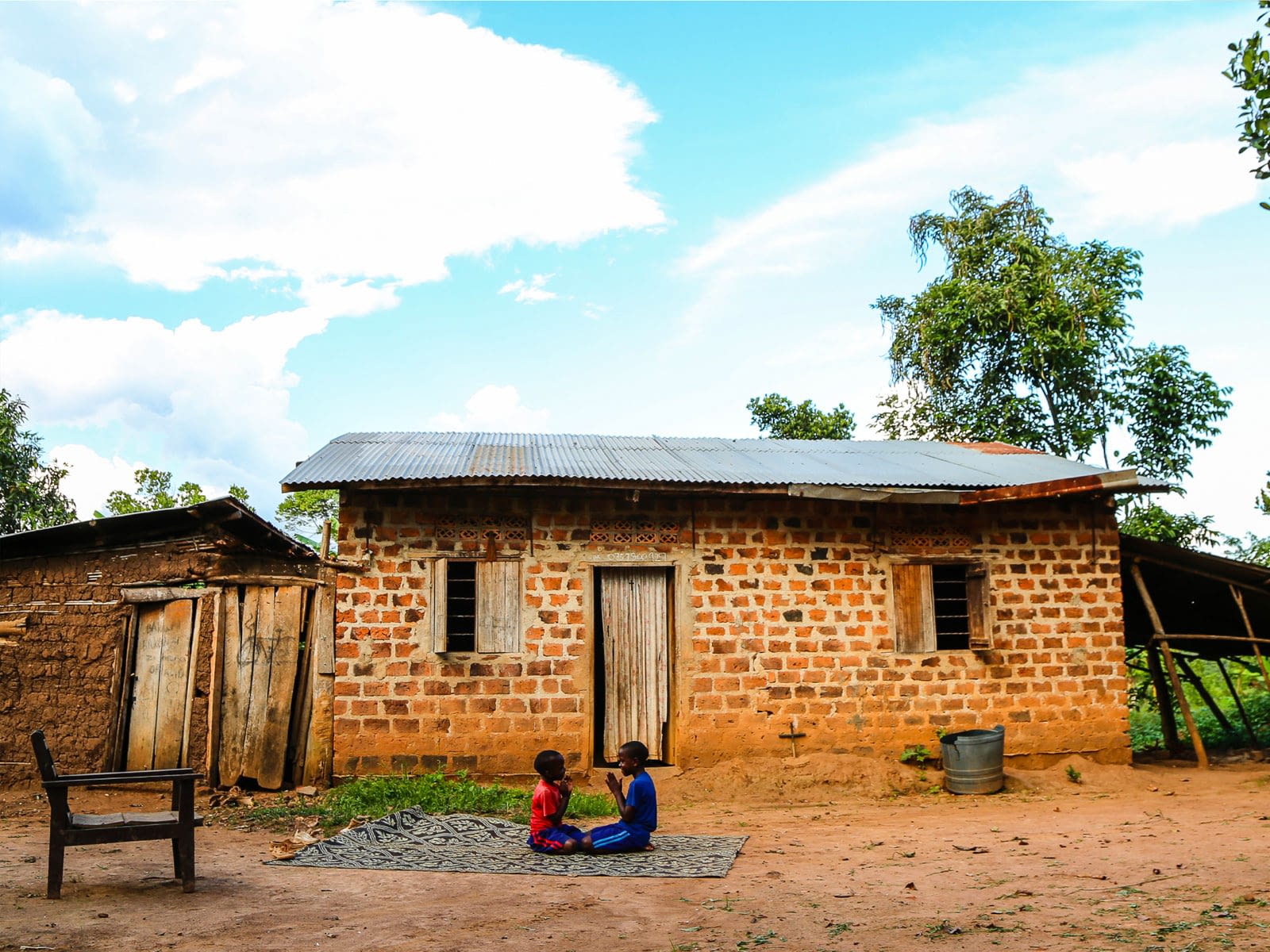 Two children playing on a rug outdoors in their village