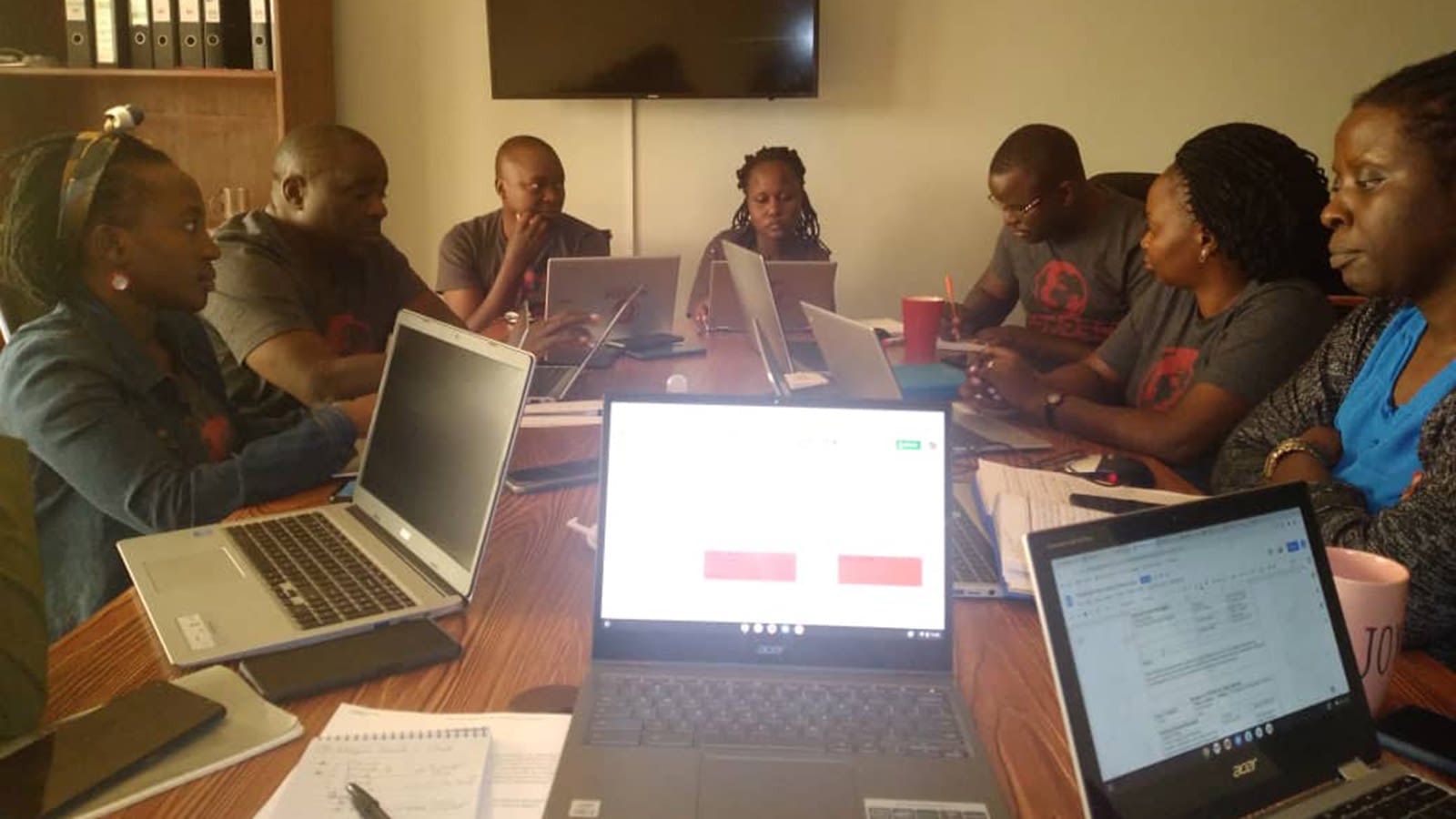 Team members meet around a table with laptops and papers out.