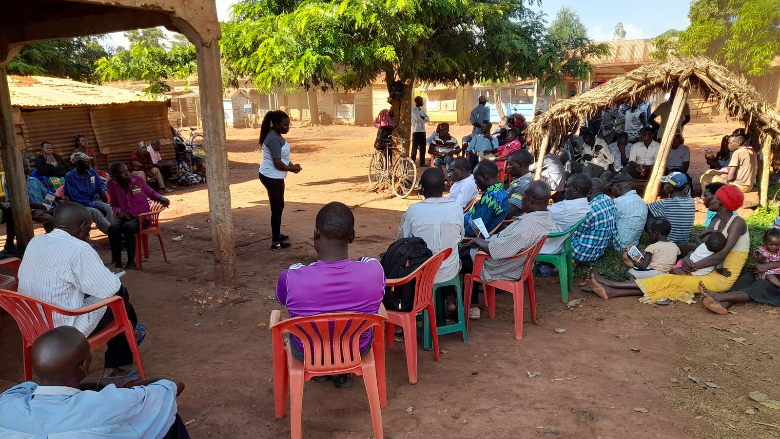 Woman speaks to a small crowd of people sitting in plastic chairs.