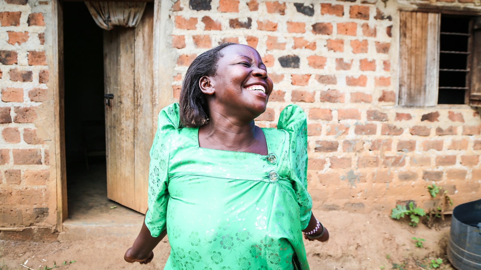 Woman with a big smile stands in front of a home with her arms stretched back.