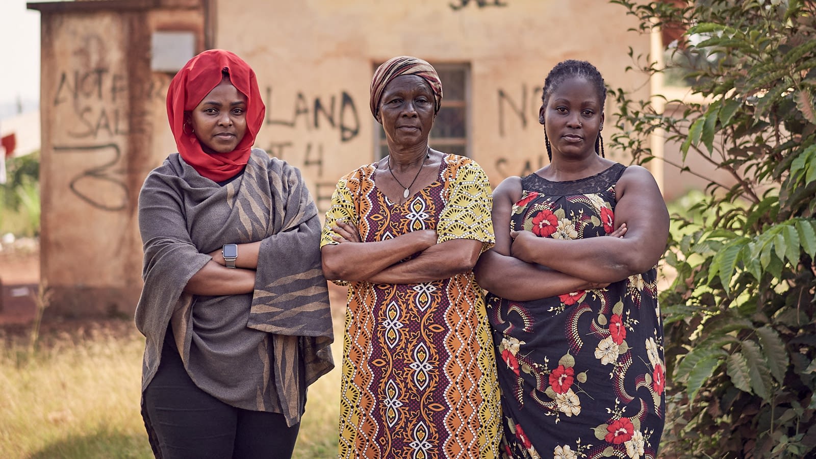 Three woman stand facing the camera with their arms crossed looking serious.