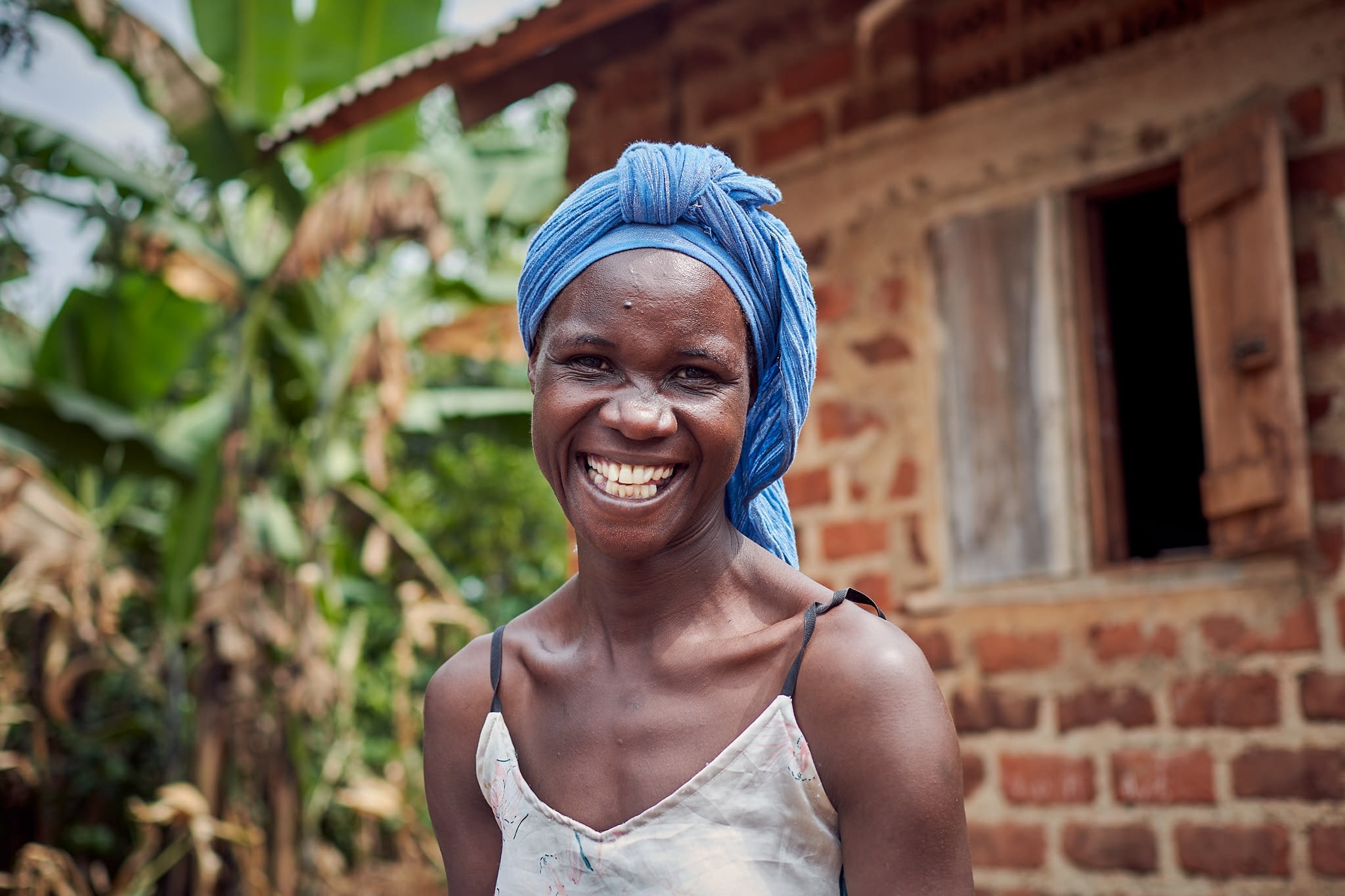 Picture of Ugandan widow smiling with her home in the background