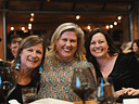 Three smiling women posing together at a dinner event