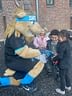Moose mascot greets three smiling children outside brick building