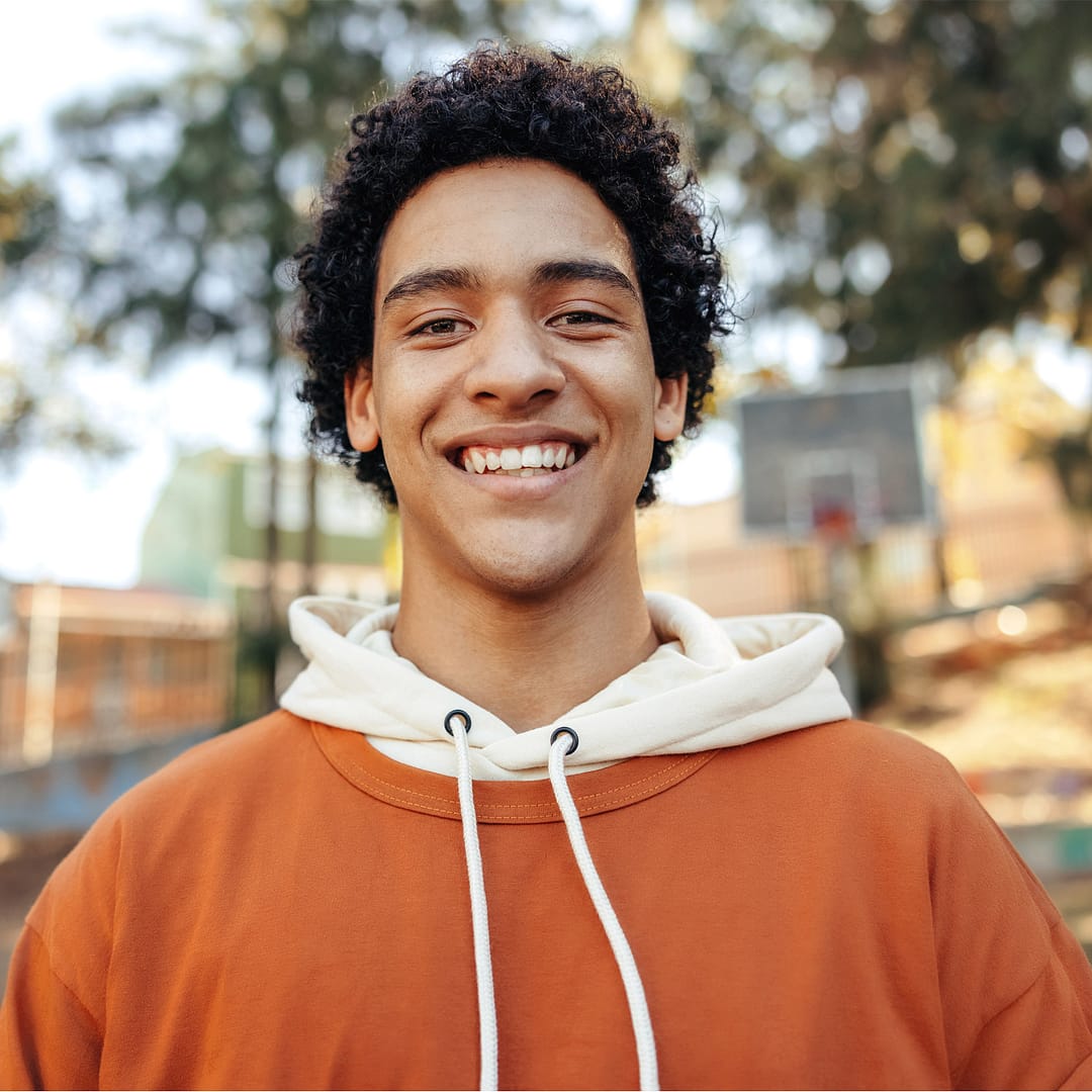 Teenage boy in orange sweatshirt smiles for the picture.