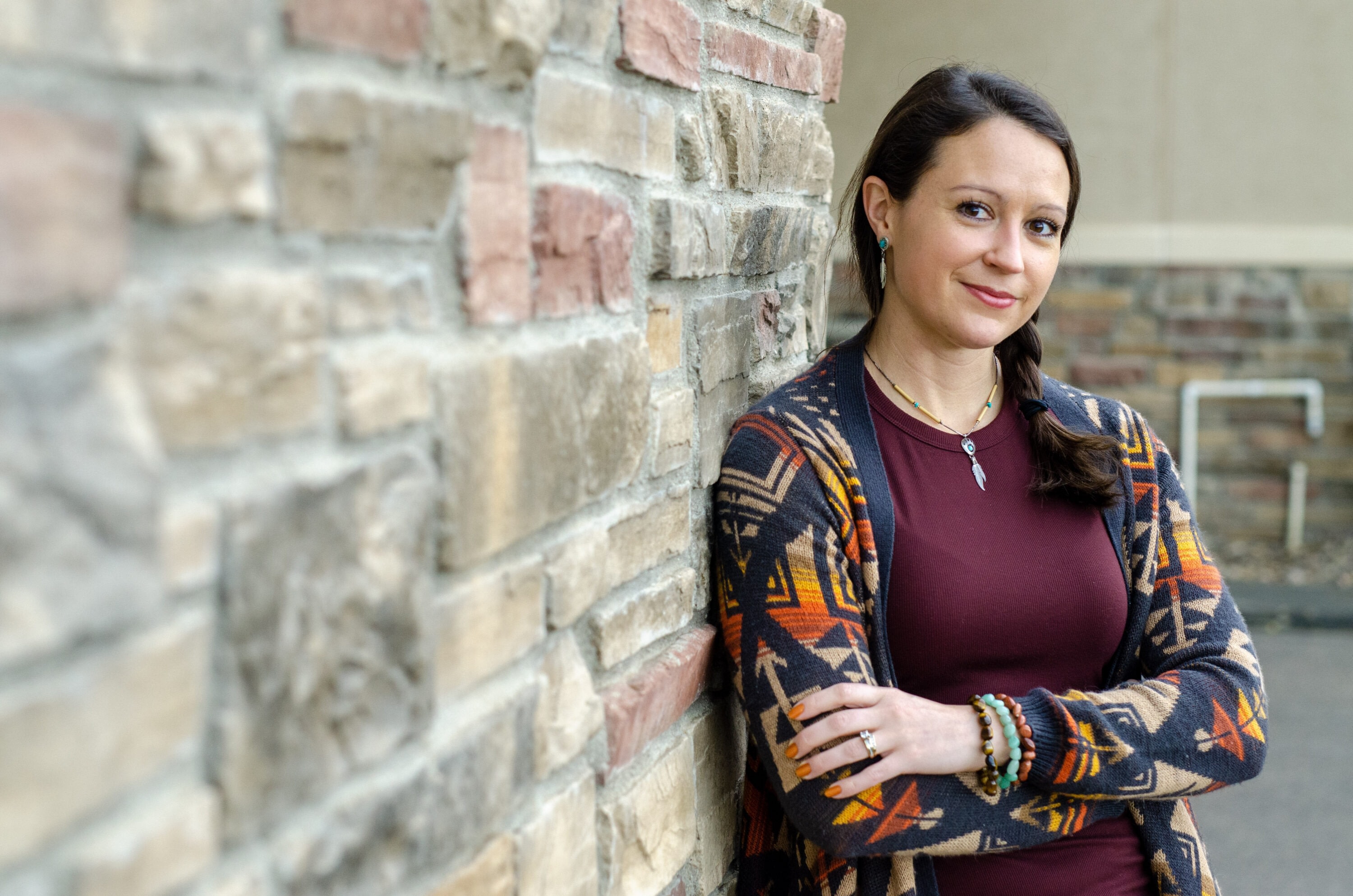 Woman in patterned cardigan leans against a brick wall