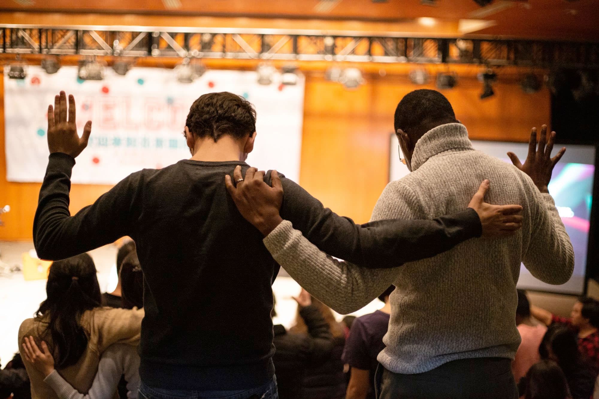 Two men with their arms on each other's shoulders at a church prayer service