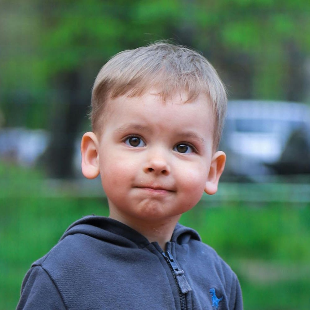Smiling toddler wearing a gray hoodie outdoors