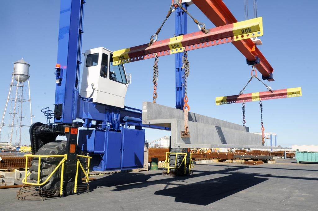 Heavy machinery lifting concrete beam at construction site.