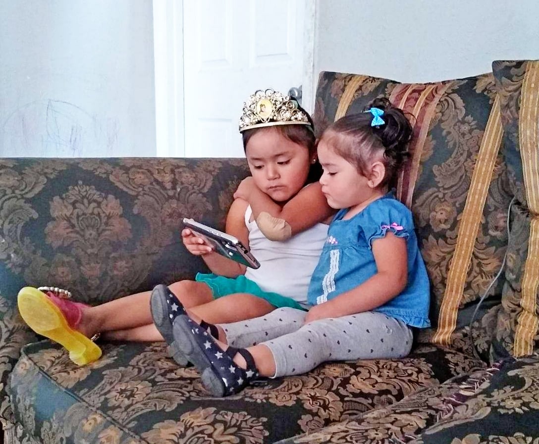 Two kids sitting on a couch, one with a crown.