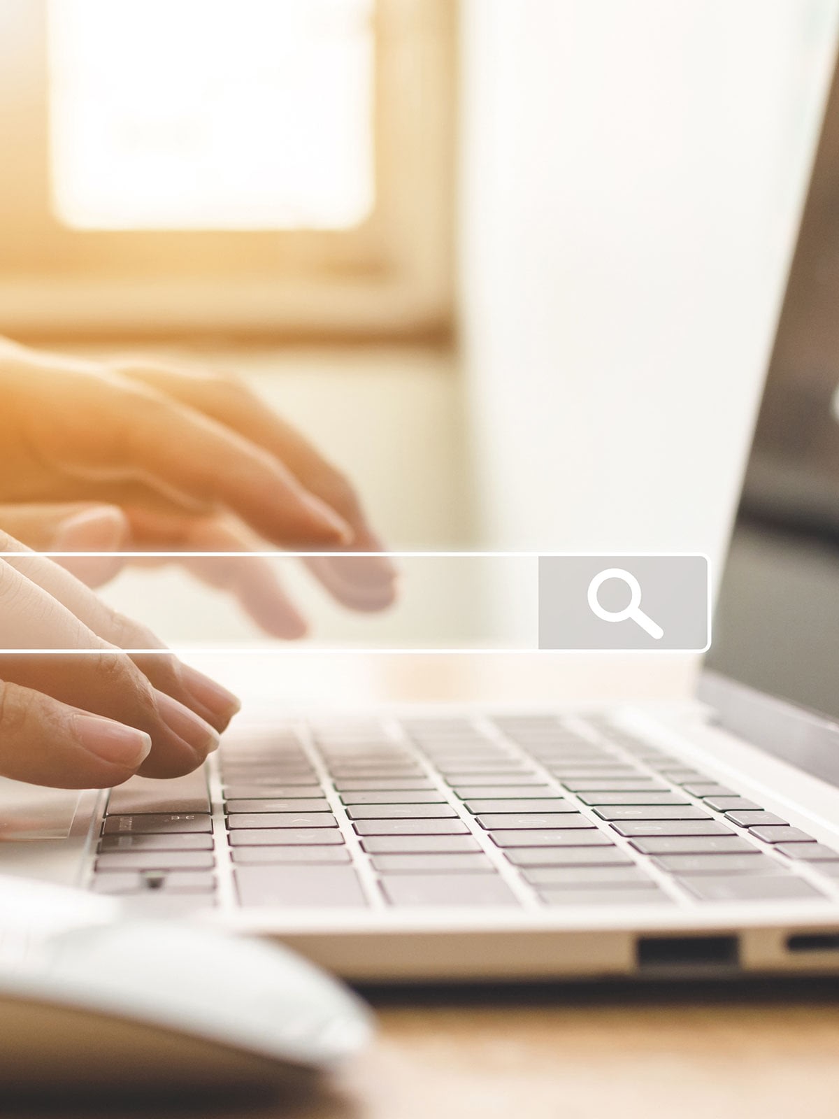 Hands typing on laptop keyboard, search icon overlay.