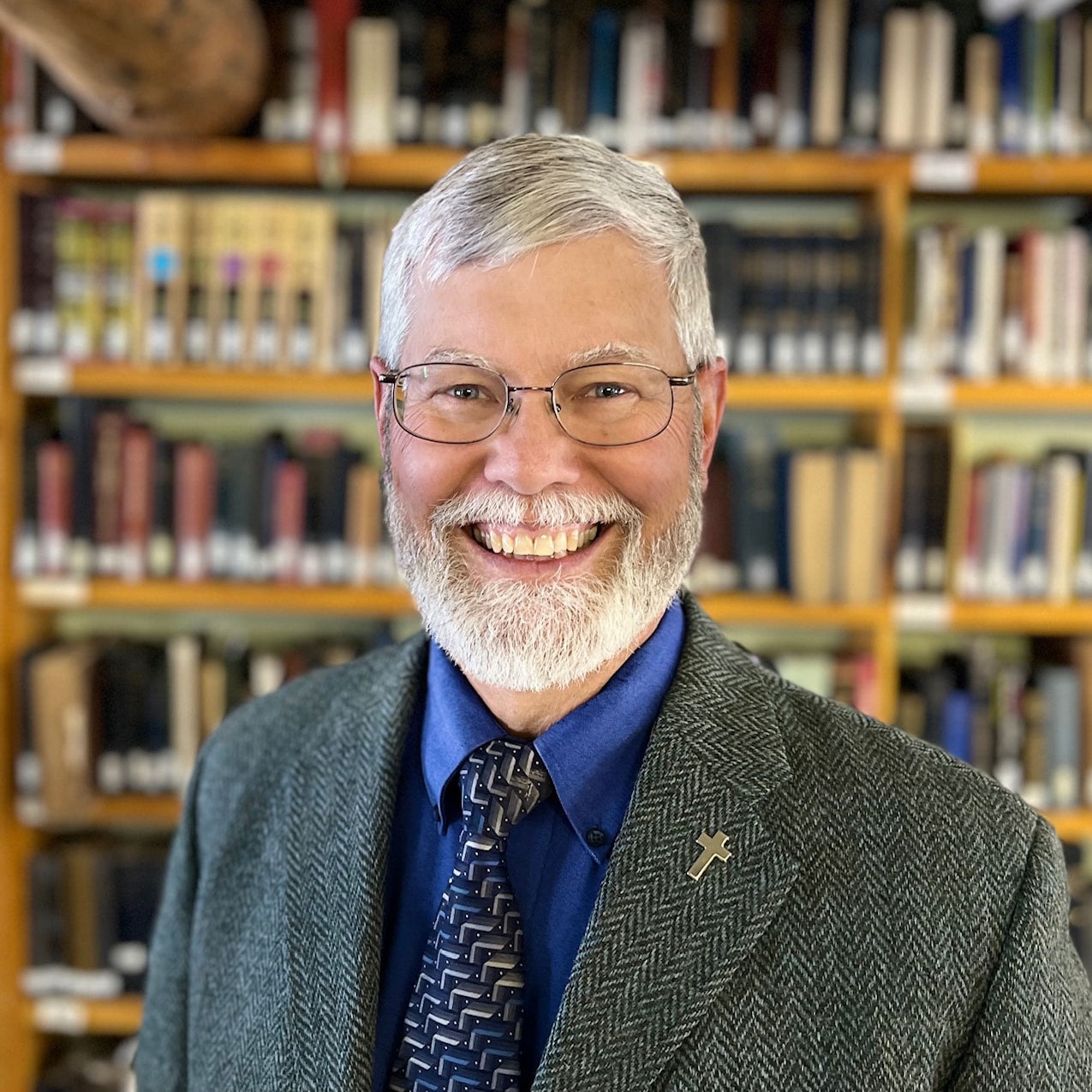 Smiling bearded man in suit before bookshelves