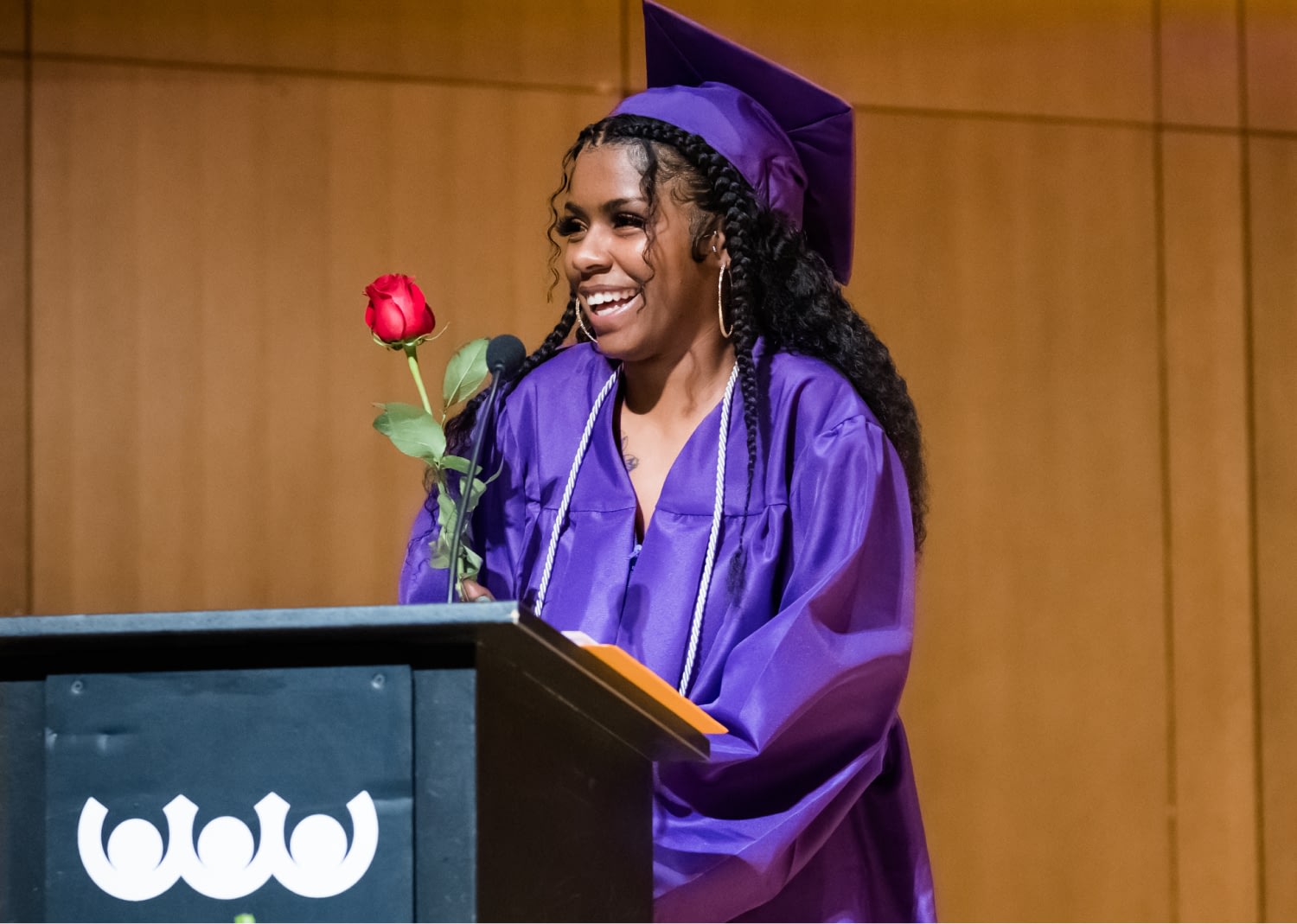 Graduate smiling with rose during ceremony speech.