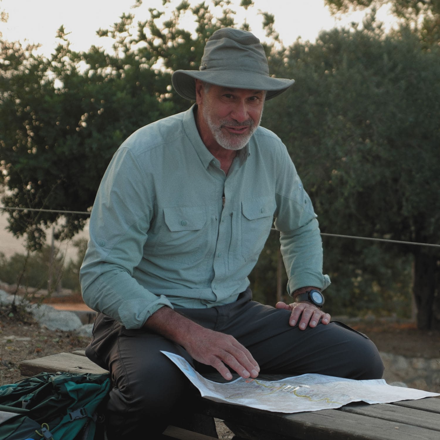 Man studying map outdoors, wearing hat and watch.