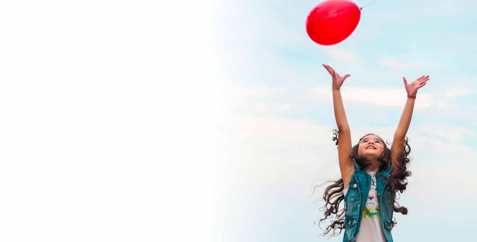 Smiling child releases red balloon outdoors