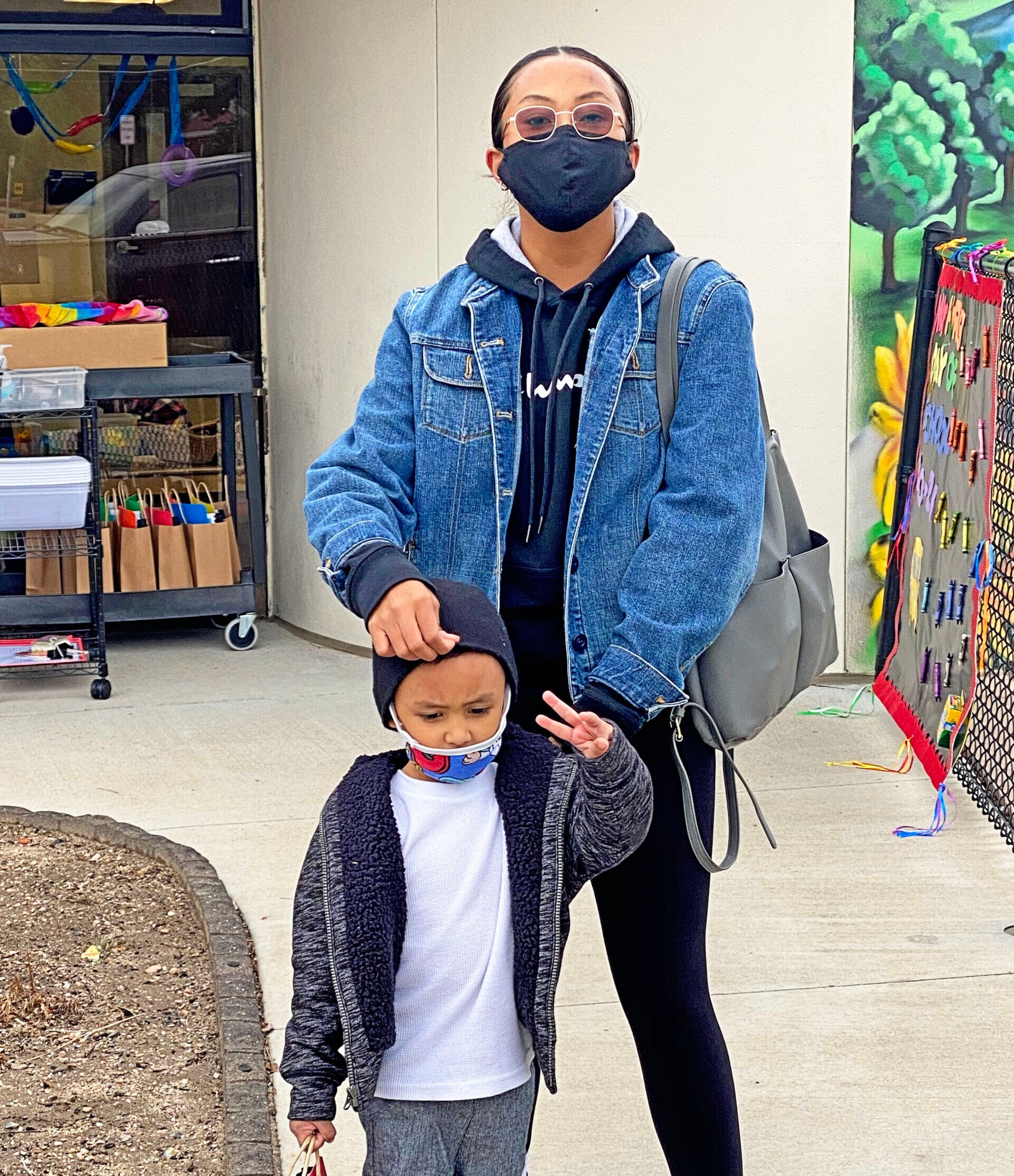 Masked woman with child at school entrance.
