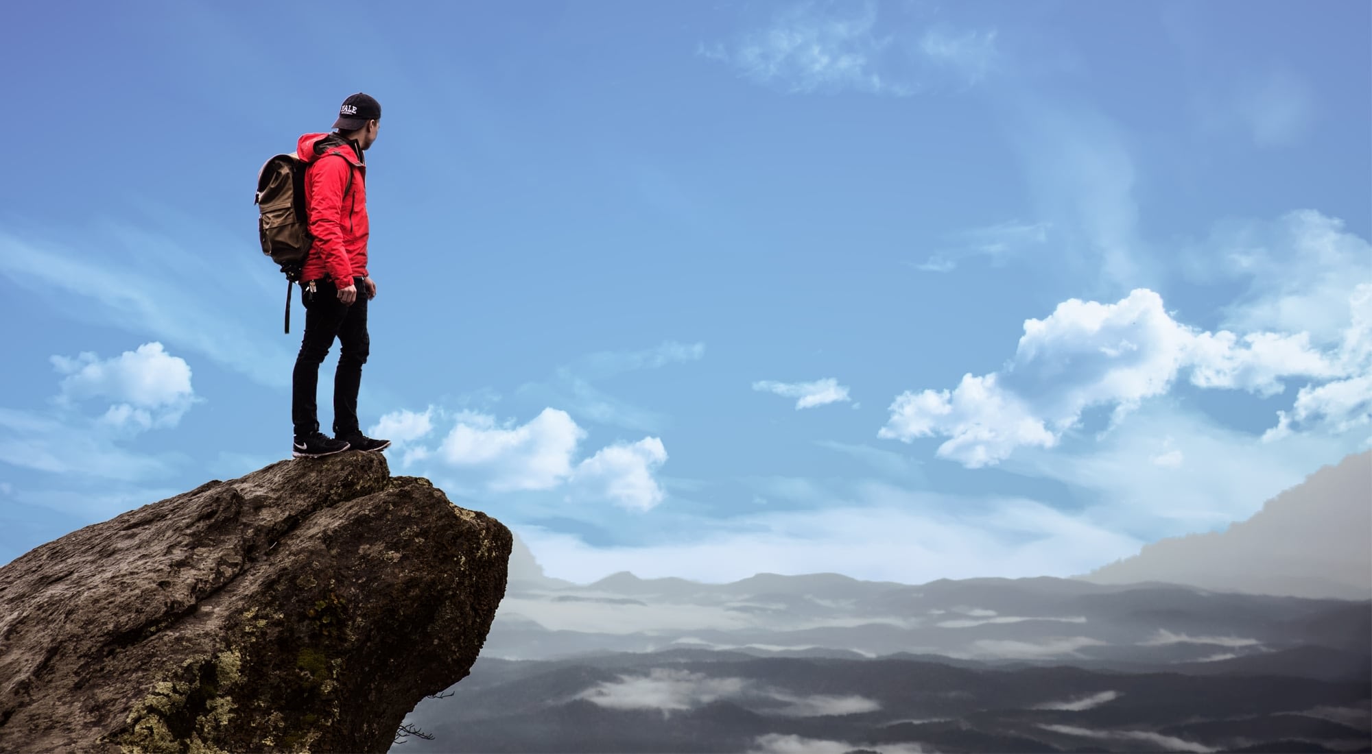 Hiker standing on cliff overlooking mountains