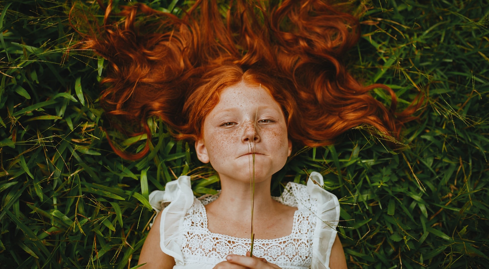 Girl with red hair lying on green grass