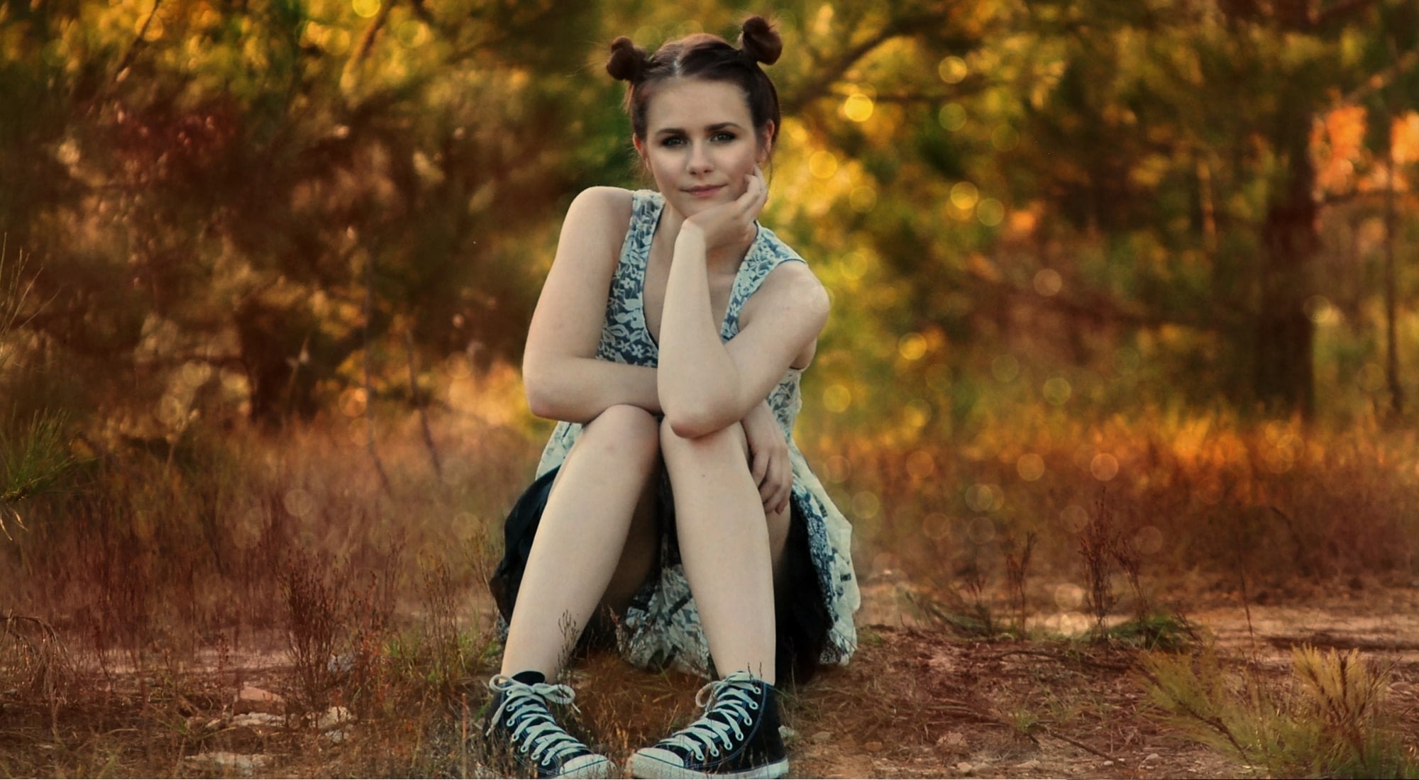 Young woman sitting on forest ground at sunset