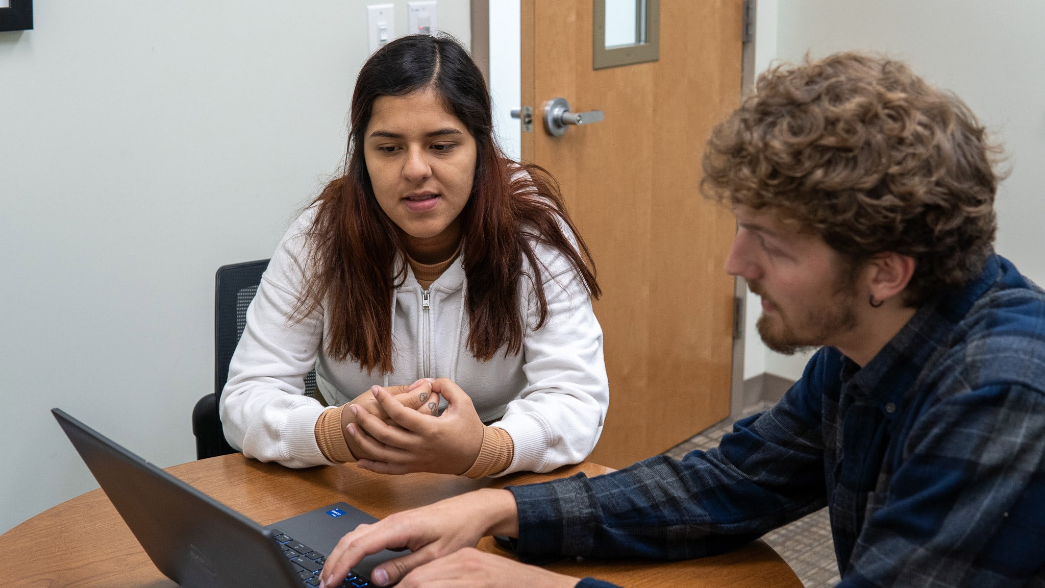Two people collaborating on laptop at desk.