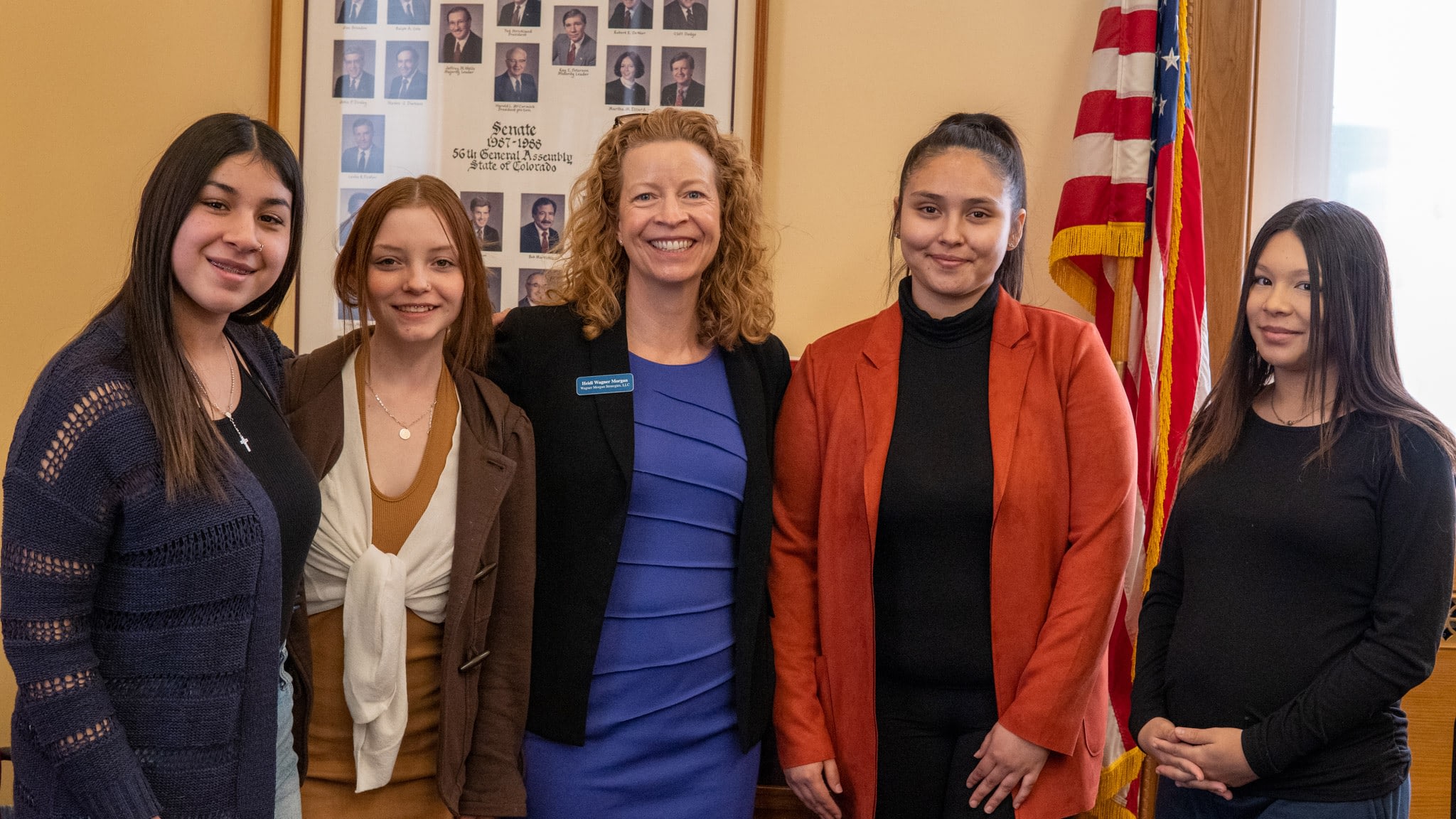 Group smiling in front of political portraits and flag