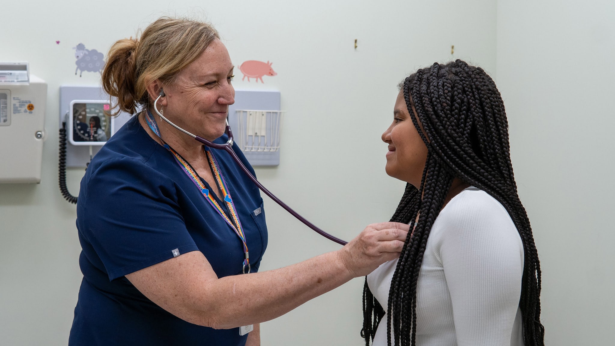 Nurse using stethoscope on patient in exam room.
