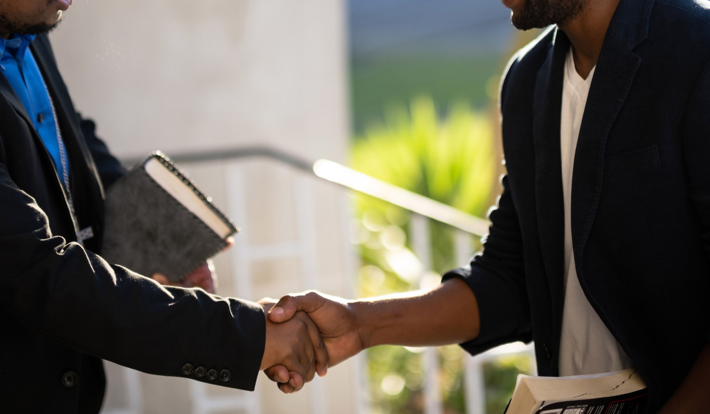 Two men shaking hands and smiling outdoors.