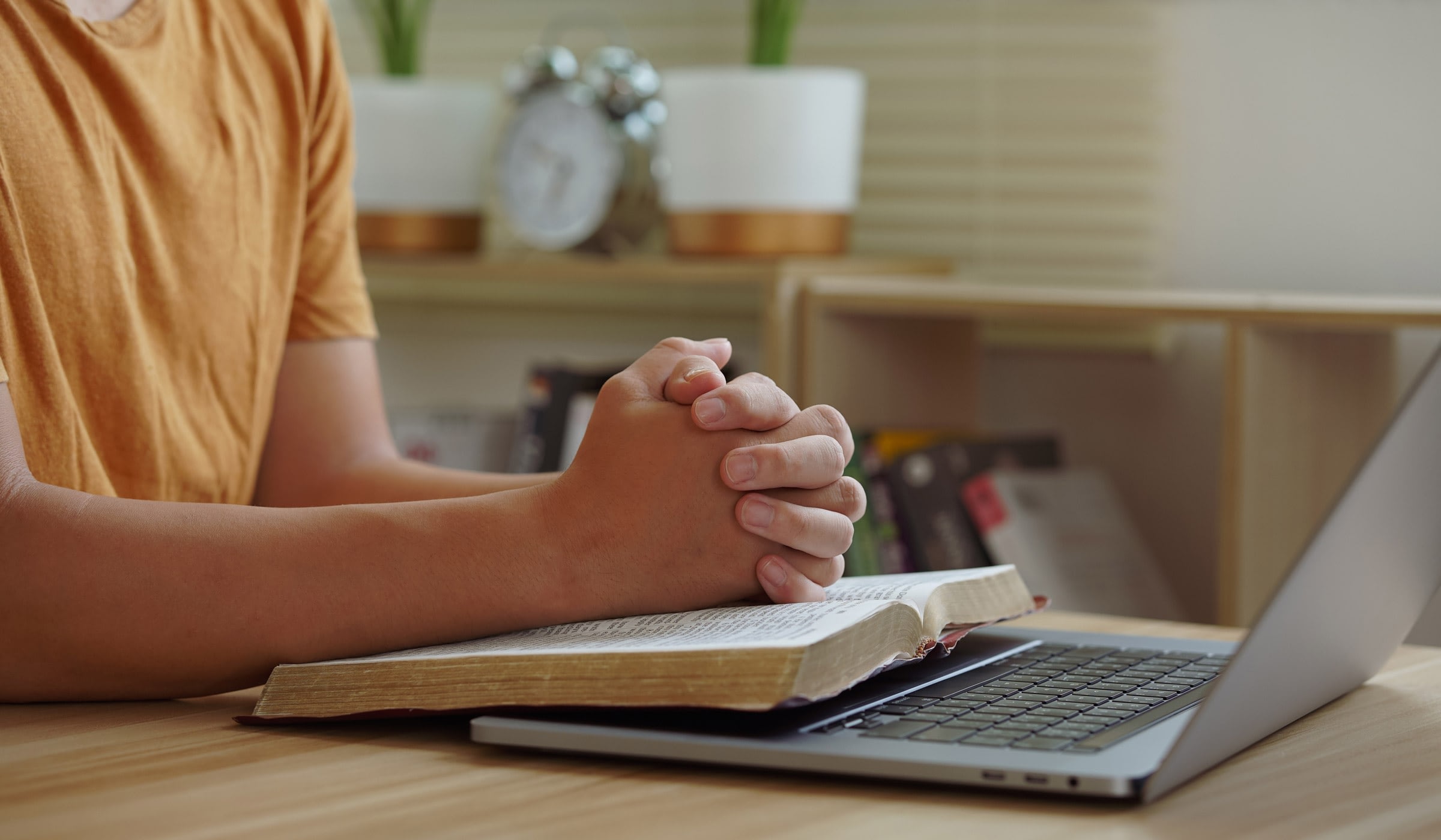 Person praying with open book and laptop