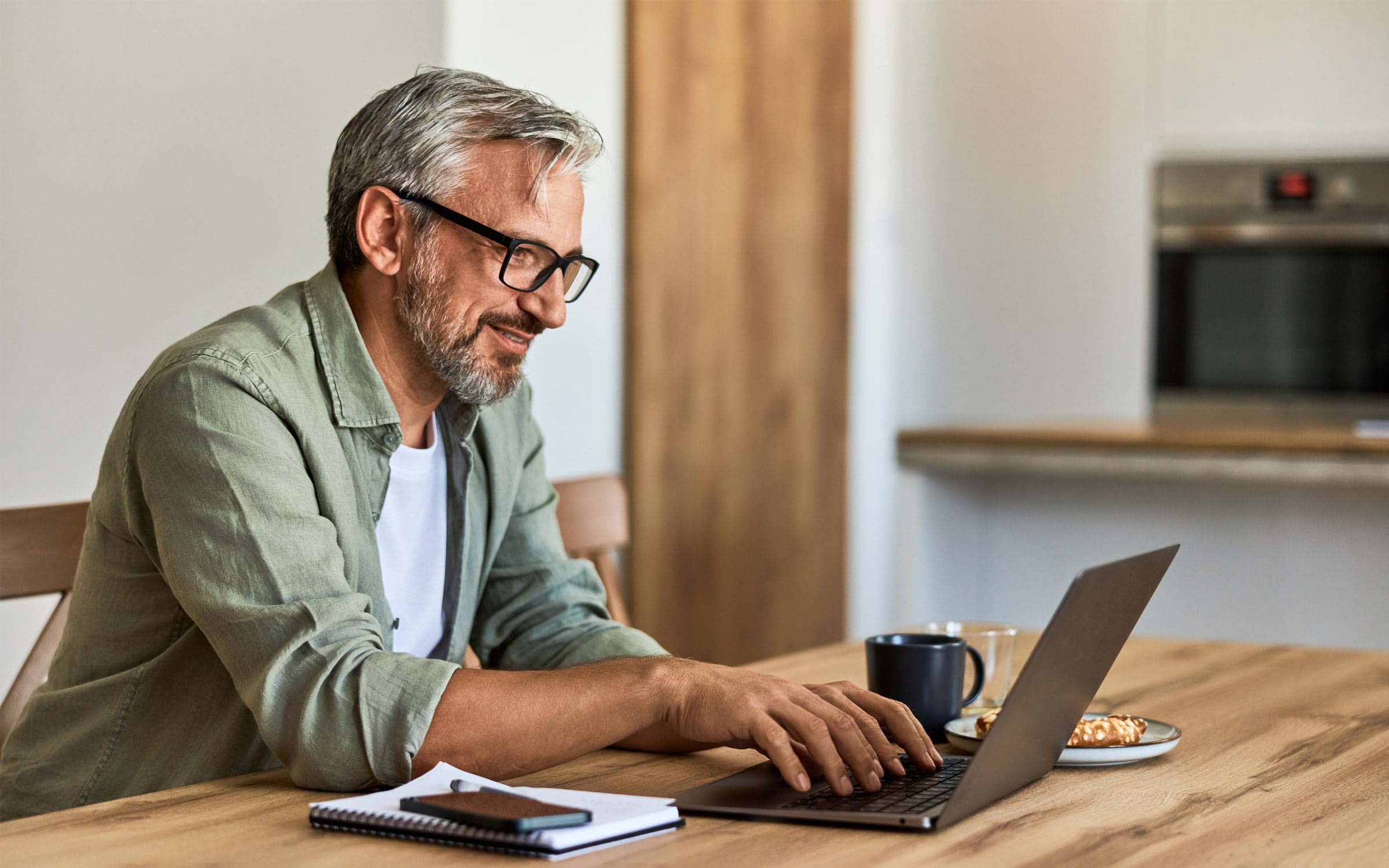 Man working on laptop at home kitchen table.