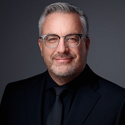 Professional headshot of gray-haired man wearing glasses and black suit