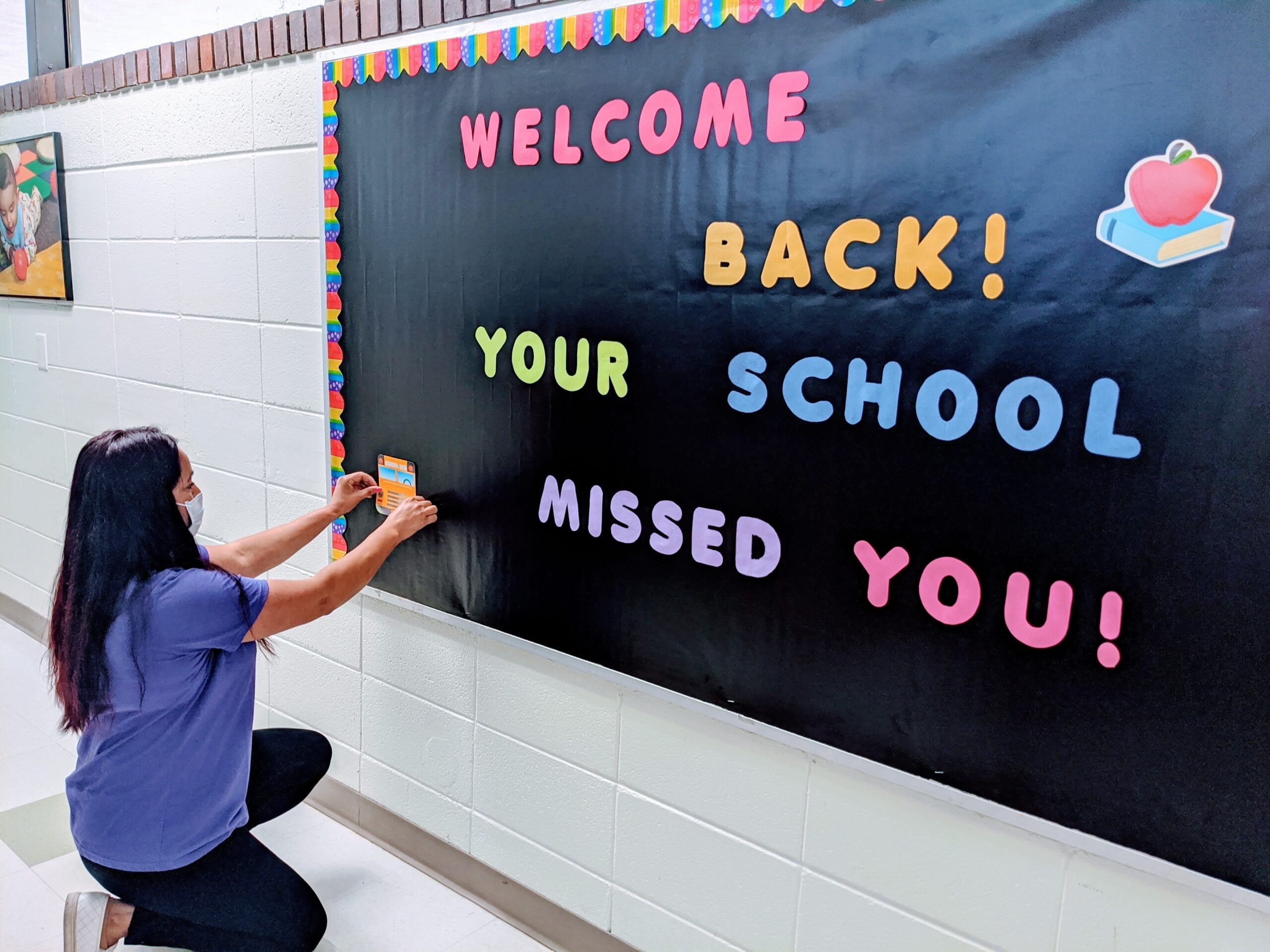Teacher decorating welcome back school bulletin board.