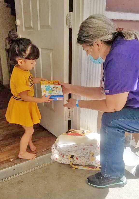 Woman giving toy box to child at door.