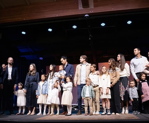 A diverse group of families with young children standing on a church stage during a child dedication service or family presentation.