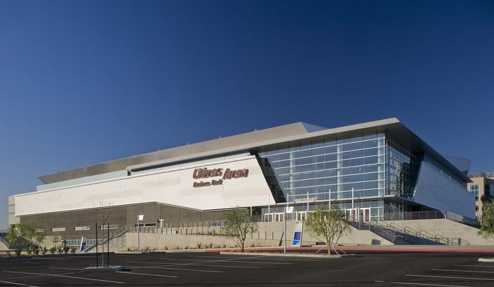 Modern arena building with glass facade and clear sky.