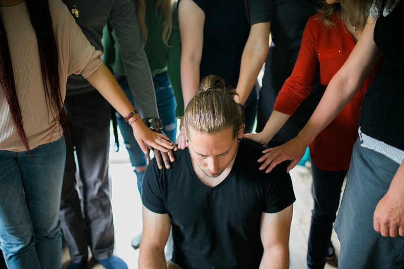 Group of young people's hands in a circle praying over man with ponytail