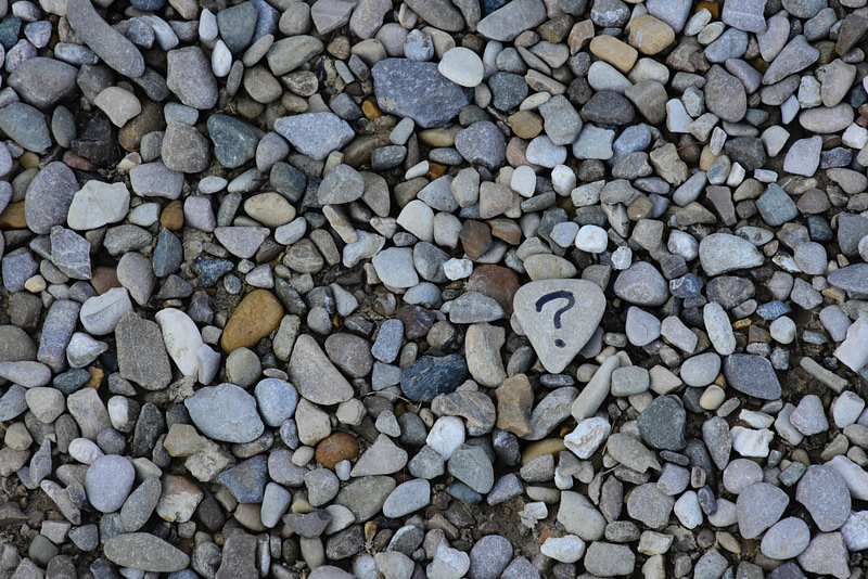 Many small stones in a pile with one marked with a question mark